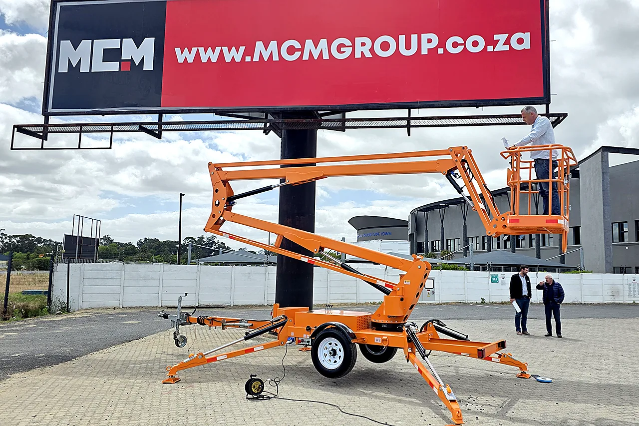 Technician in the basket of an MCM towable cherry picker working beside an MCM billboard